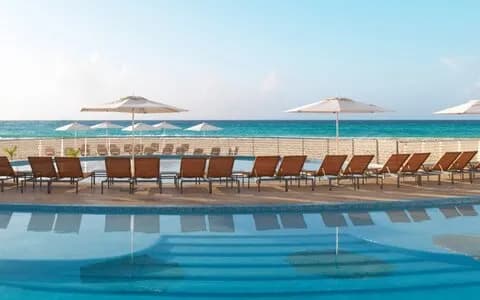 A swimming pool with a row of lounge chairs look onto the sea at Playacar Palace.